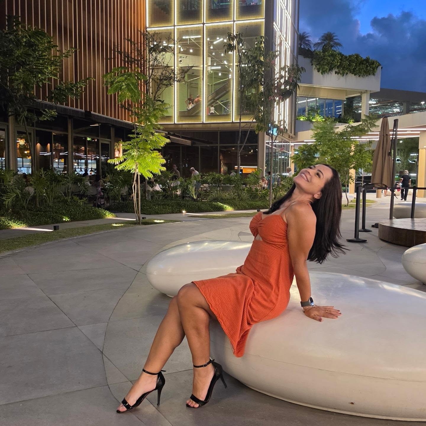 Iza Freitas sentada em ambiente externo, usando vestido laranja